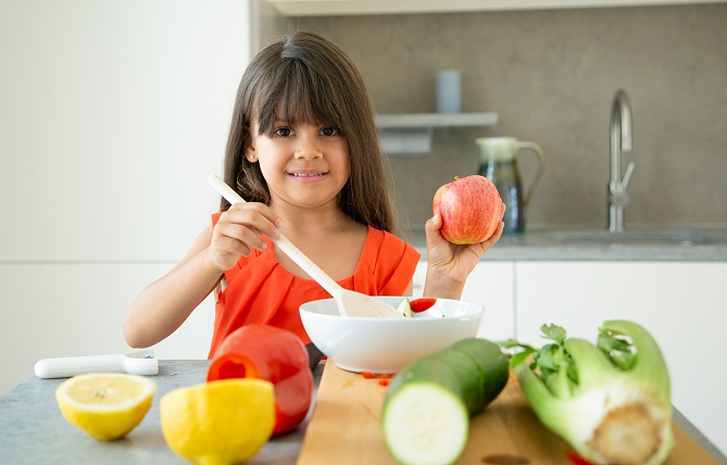 Happy girl holding apple while stirring salad